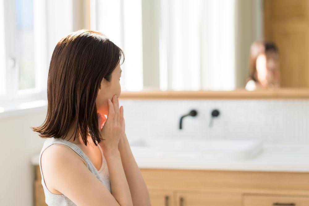 洗面台の鏡越しに顔周りを気にする女性